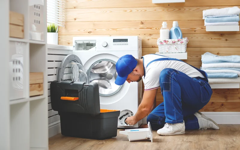 Technician in blue uniform servicing a washing machine filter in clean laundry room.