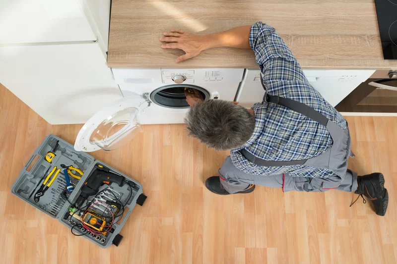 Overhead view of technician repairing a white front load washing machine with tools. Overhead view of technician repairing a white front load washing machine with tools.
