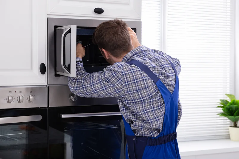 Technician in blue overalls working on a built-in microwave in kitchen