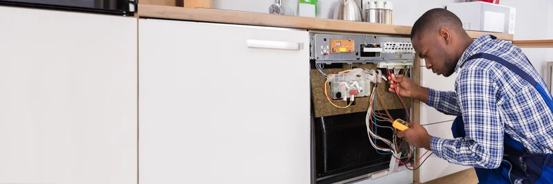 Appliance repair technician diagnosing a kitchen dishwasher with a multimeter.