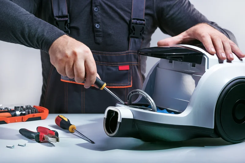 Technician repairing a canister vacuum cleaner at a work bench with tools