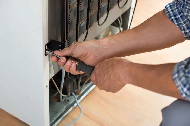 Close up of hands repairing refrigerator back panels with hand tool.