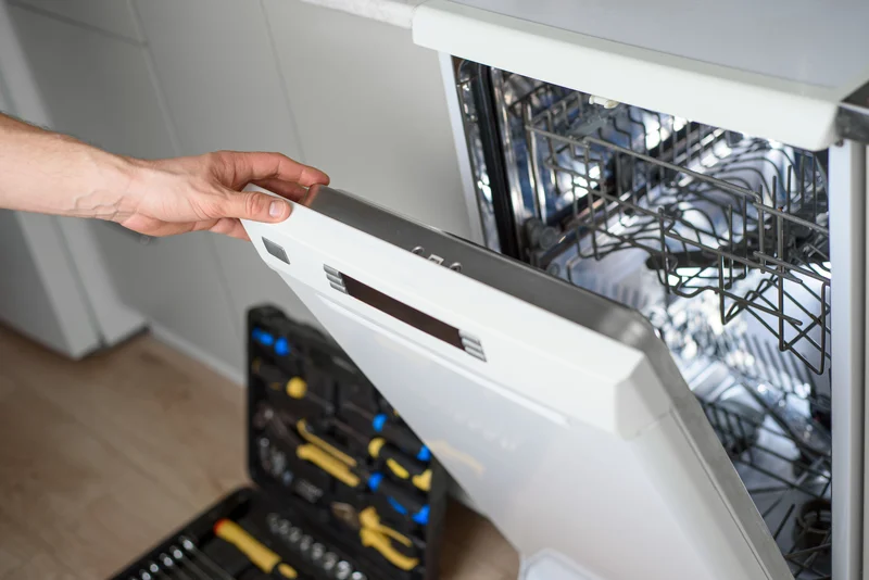 Professional repairman inspecting a kitchen dishwasher with tools
